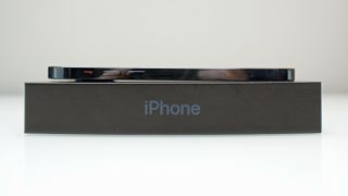 An iPhone 12 Pro viewed from the side, resting on its box