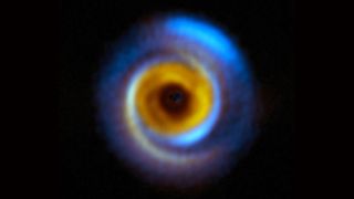A composit image of a planet-forming disk in deep space with blue and yellow hues of different wavelengths.