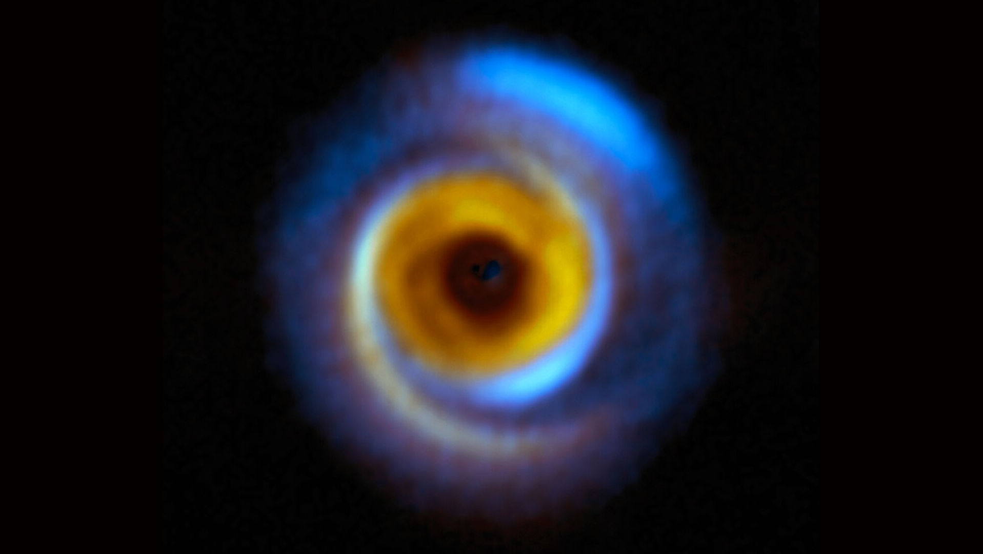 Una imagen compuesta de un disco de formación de planetas en el espacio profundo con tonos azules y amarillos de diferentes longitudes de onda.