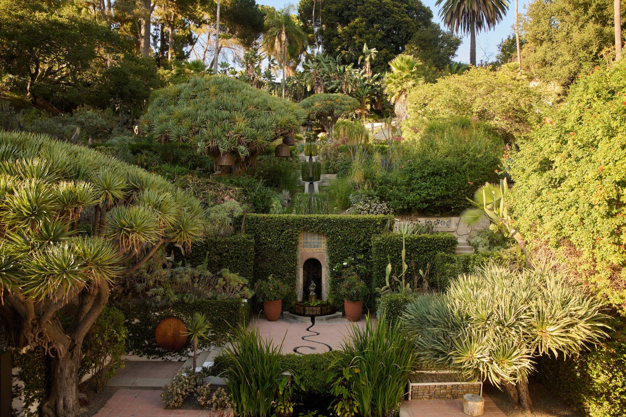 Exapnsive garden that is built on a hill and has multiple layers, covered in tres and bushes.