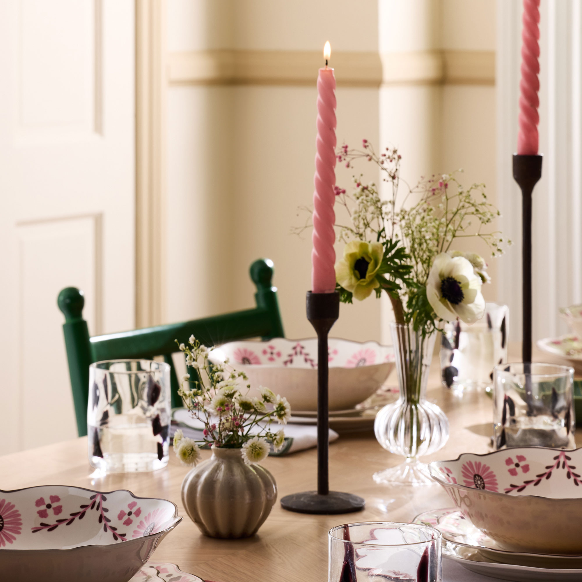 Wooden table laid with pink and red patterned crockery and pink twisted candles in black candlesticks