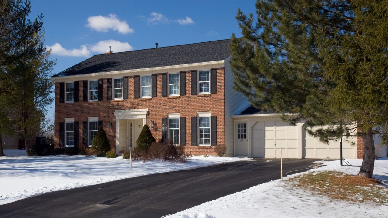 A classic red brick colonial house in the winter with no ice on the driveway