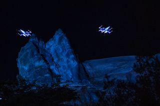 two illuminated spaceships rise above a mock mountain range
