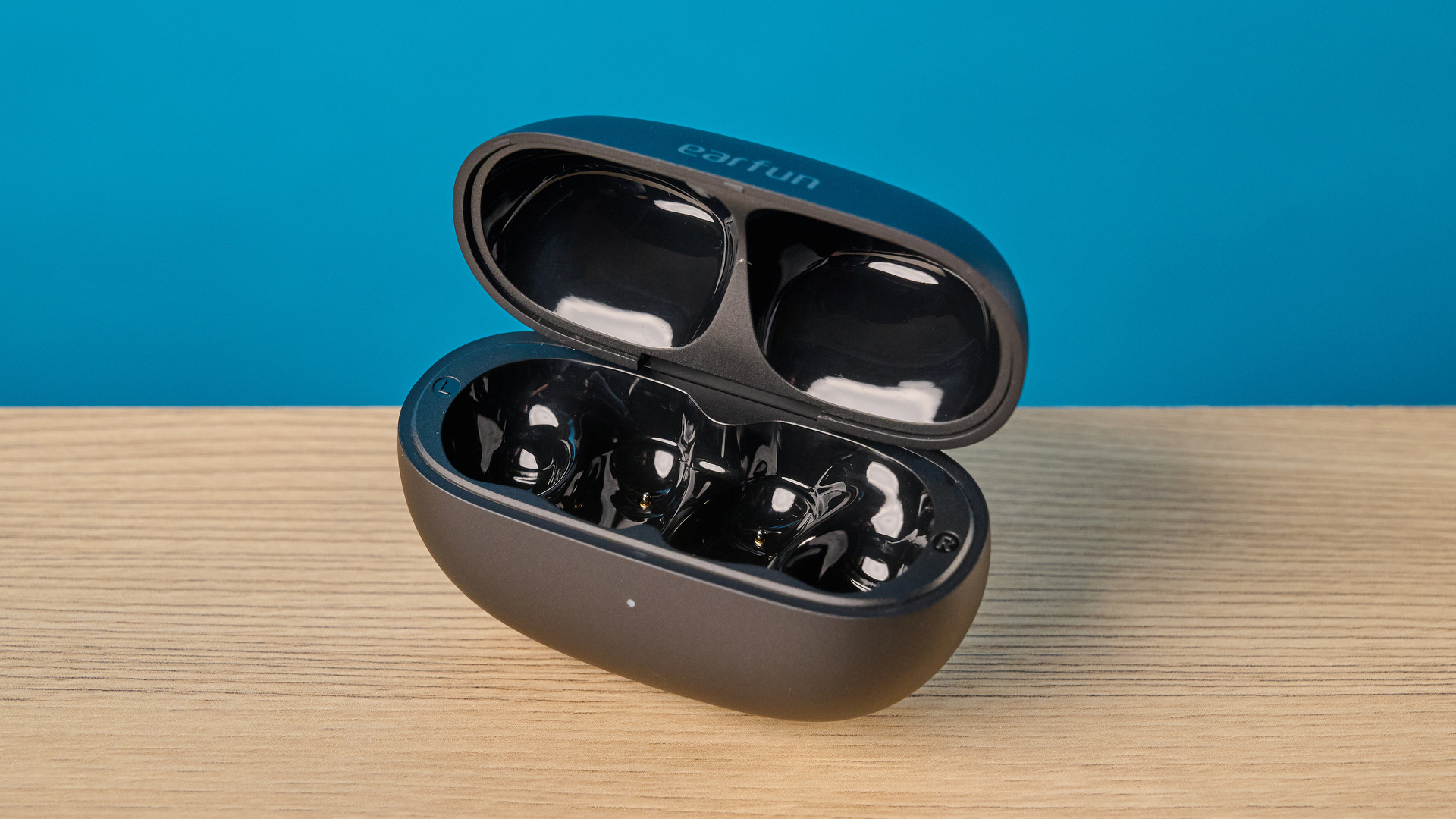 EarFun Clip 2 in black on table photographed in front of a blue background