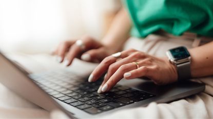A woman types on a laptop, only her hands showing.