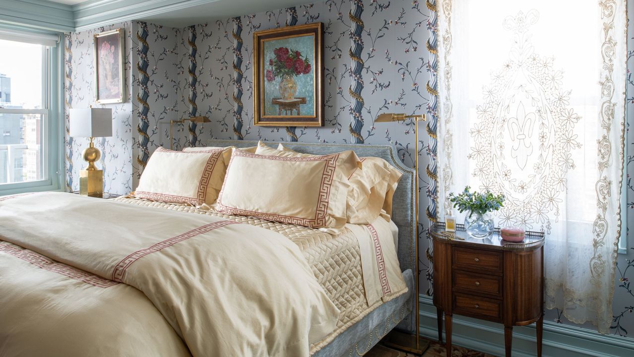 Luxe small bedroom ideas like this blue bedroom are so beautiful. This has blue wallpaper, a wooden nightstand, and a cream bed with ornate touches and detailing all around