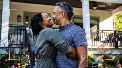 Woman and man embracing outside of a house surrounded by trees