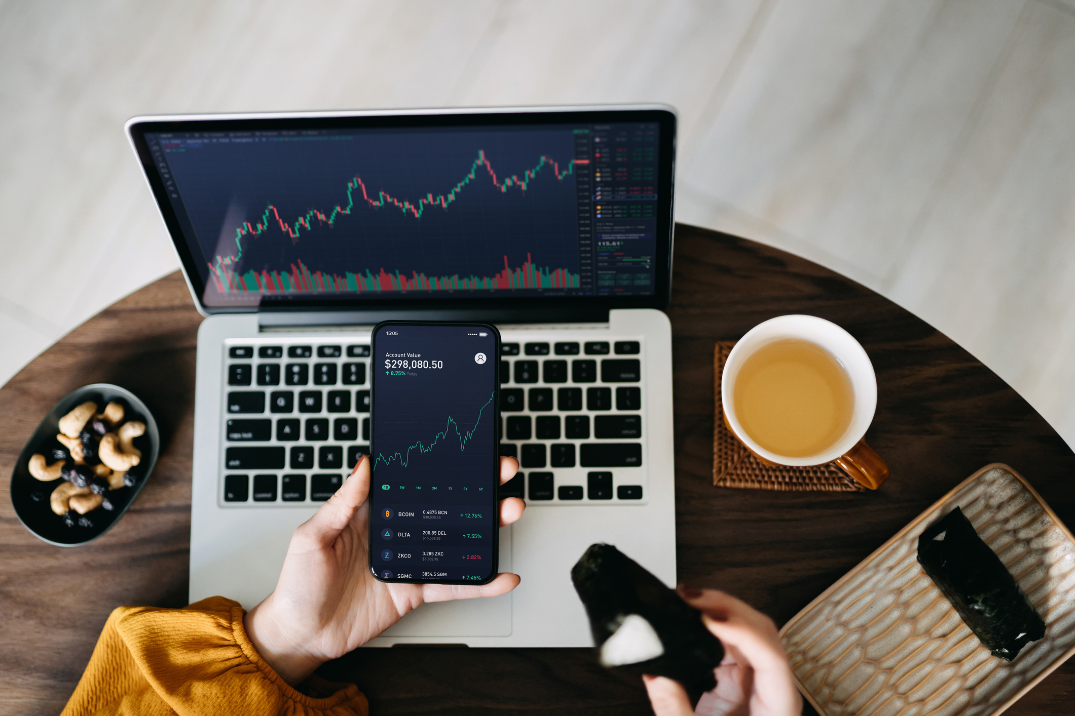 A woman holding a smartphone, analyzing investment trading data while having lunch, working at home.