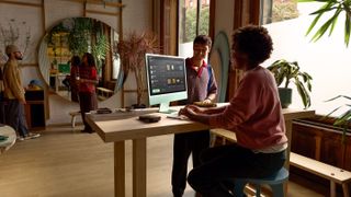 A woman working on a green M4 iMac at a desk with three other people in the background