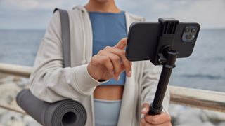 A woman tapping a smartphone on a vlogging stick