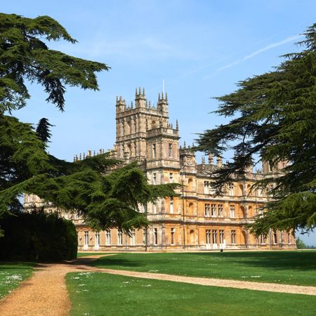 The exterior of Highclere Castle on a sunny day framed with two massive trees