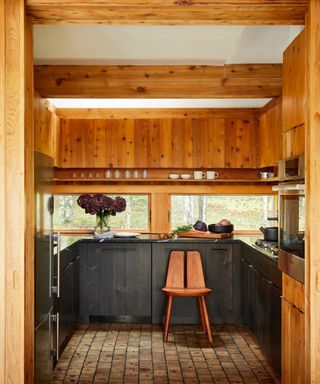 chalet style kitchen with black wood stained cabinetry, black countertops, terracotta floor tiles, chair, wood surround and shelving