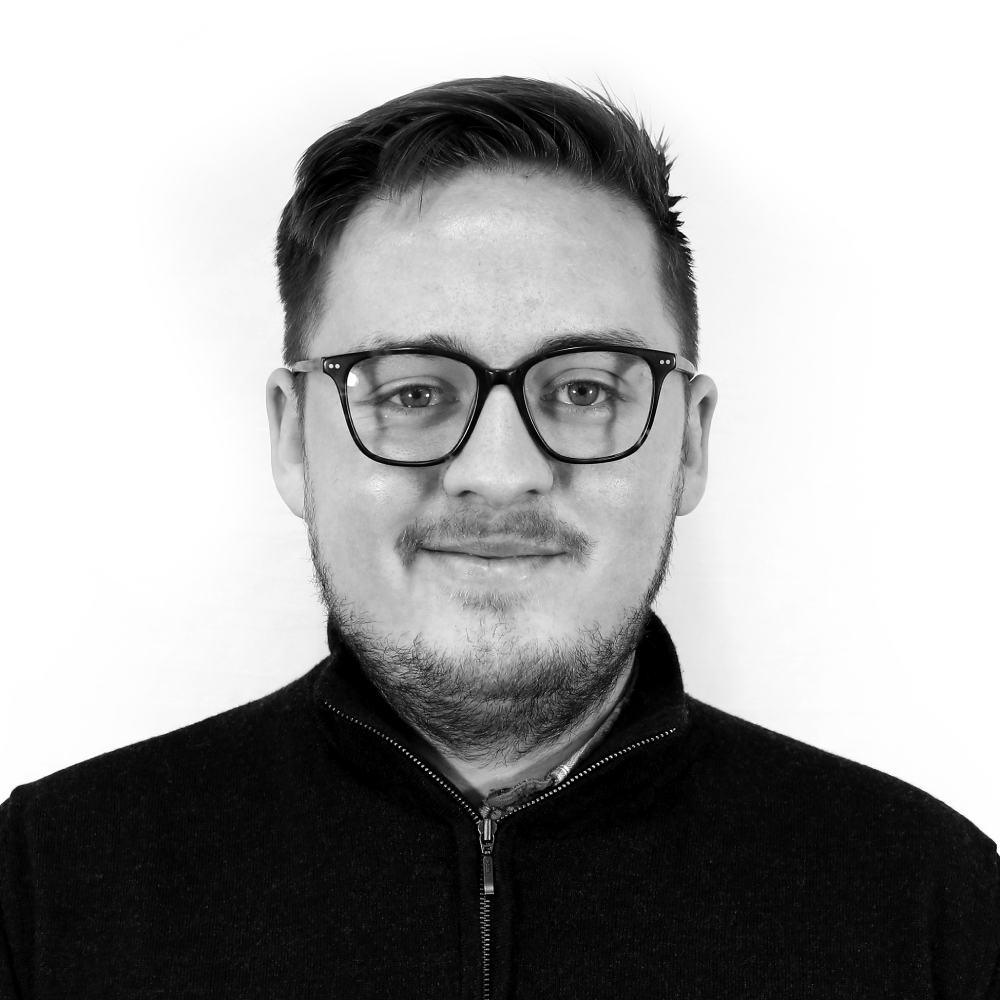 black and white photo of male with short hair, glasses, facial hear wearing dark zip up top