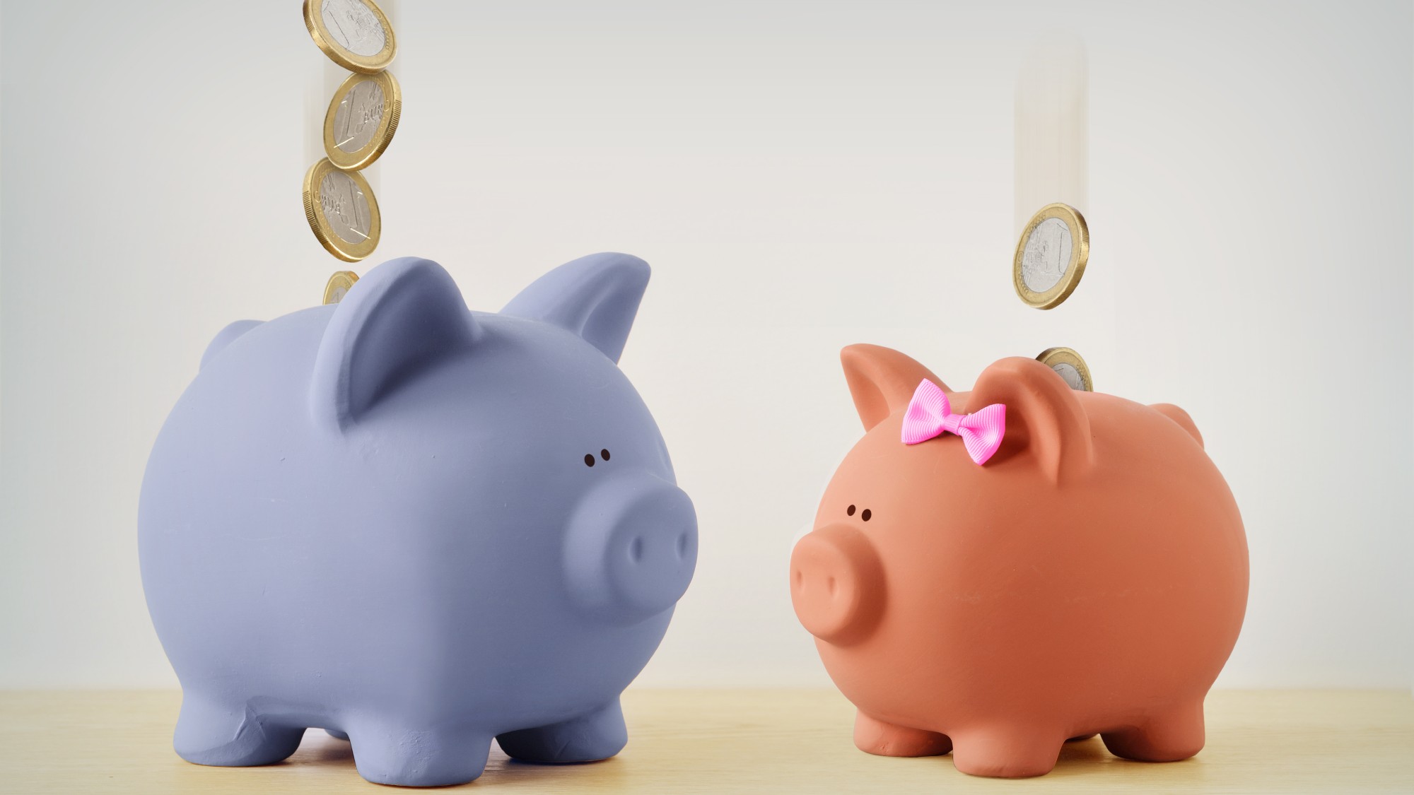 Blue piggy bank alongside a pink piggy bank wearing a bow, with coins falling into both