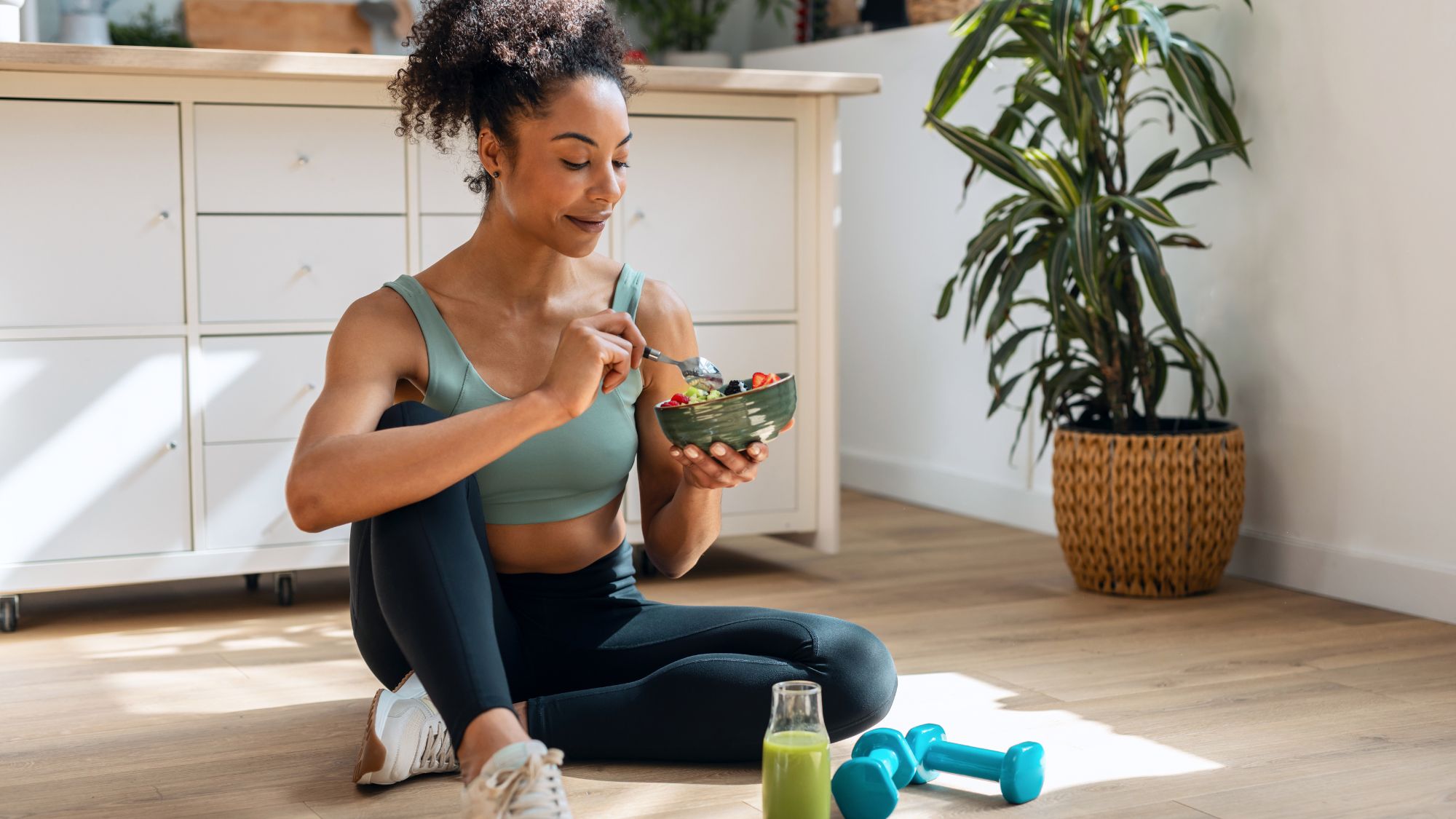 Foods that have more protein than eggs: A woman in gym kit eating a salad and drinking a green juice on her kitchen floor