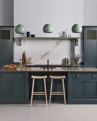 Dark gray-green painted kitchen cabinet ideas with three pale green pendant lights and pale walls and flooring.