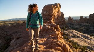 A woman hiking a trail in Arches National Park on a sunny day