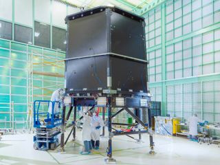 scientists in clean suits work on a large grey rectangle in a cleanroom