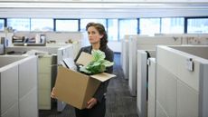 Young businesswoman in an office carrying cardboard box full of a plant and her belongings