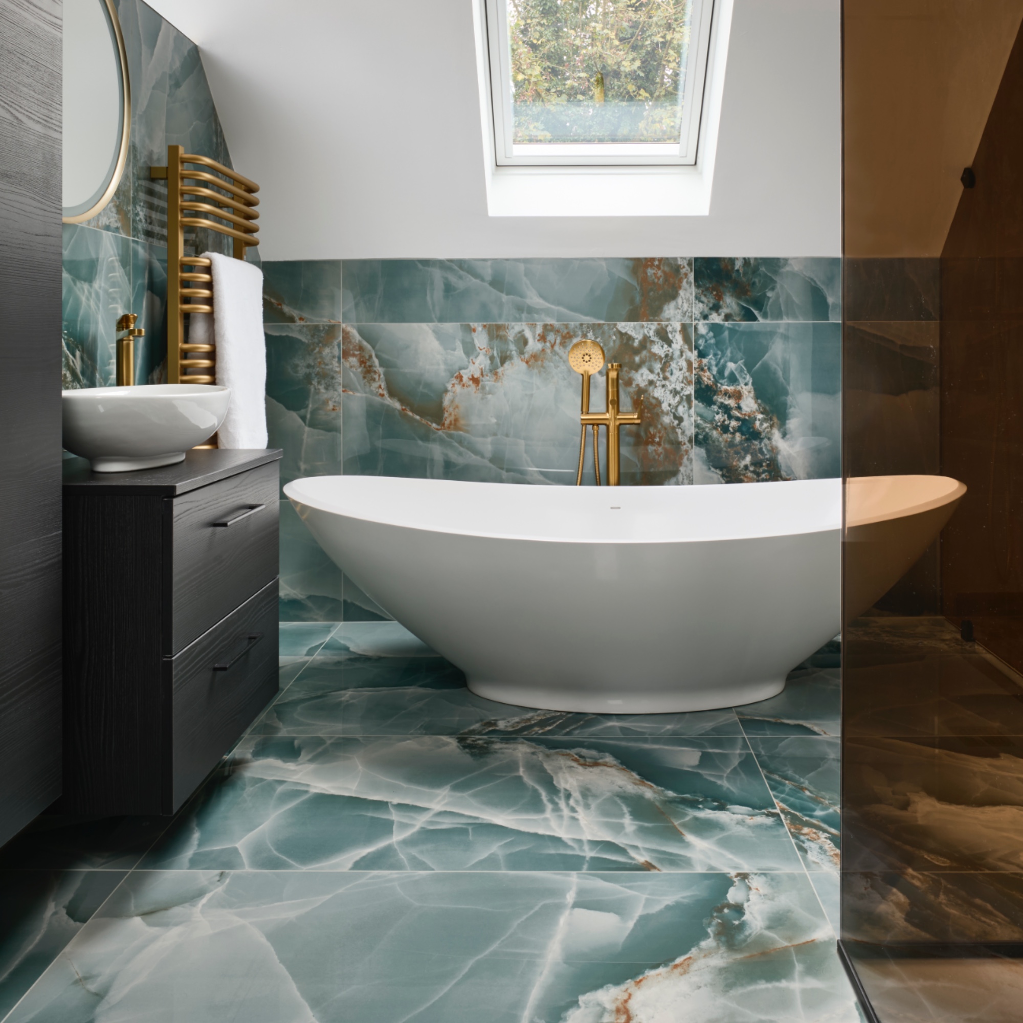 modern bathroom with large white bath, teal marble floor and wall tiles, brassware, wall mounted storage