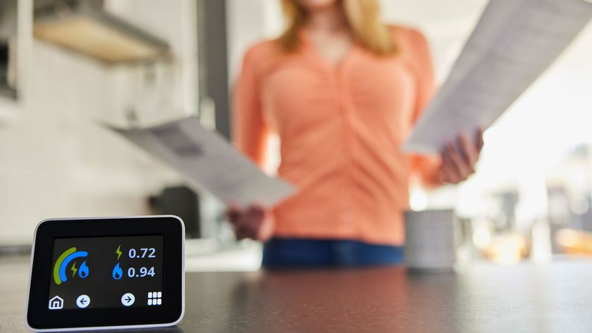 Close Up Of Smart Energy Meter In Kitchen Measuring Electricity And Gas Use With Woman Looking At Bills