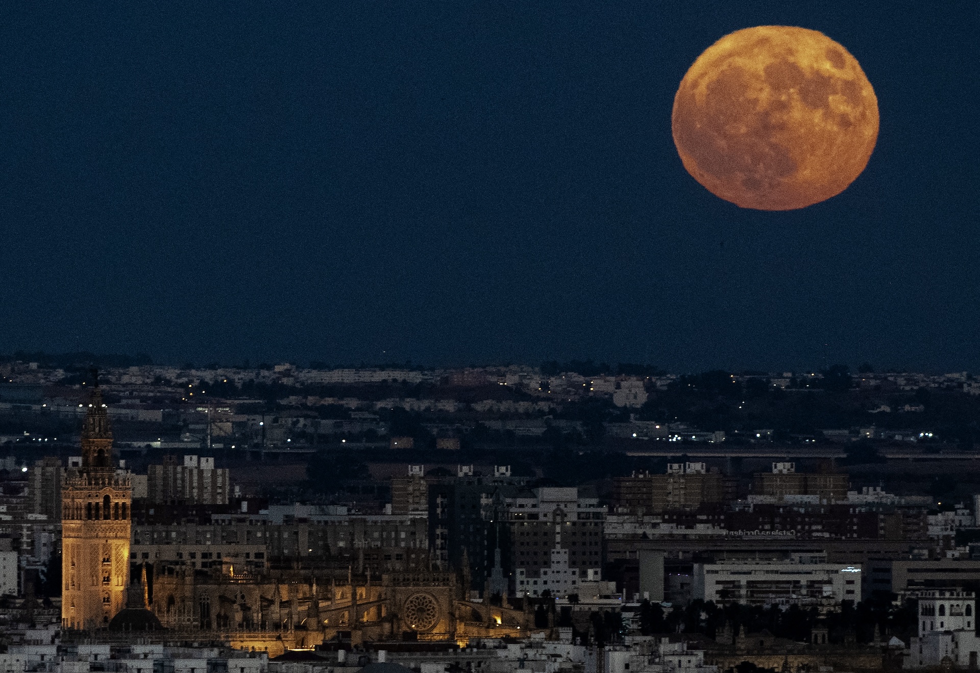 A Lua cheia nasce sobre a catedral de Sevilha e brilha com uma cor laranja empoeirada.