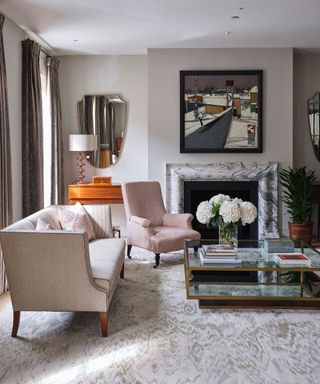 An example of neutral living room ideas with a patterned rug, glass coffee table and small ticking stripe sofa and pastel pink armchair.