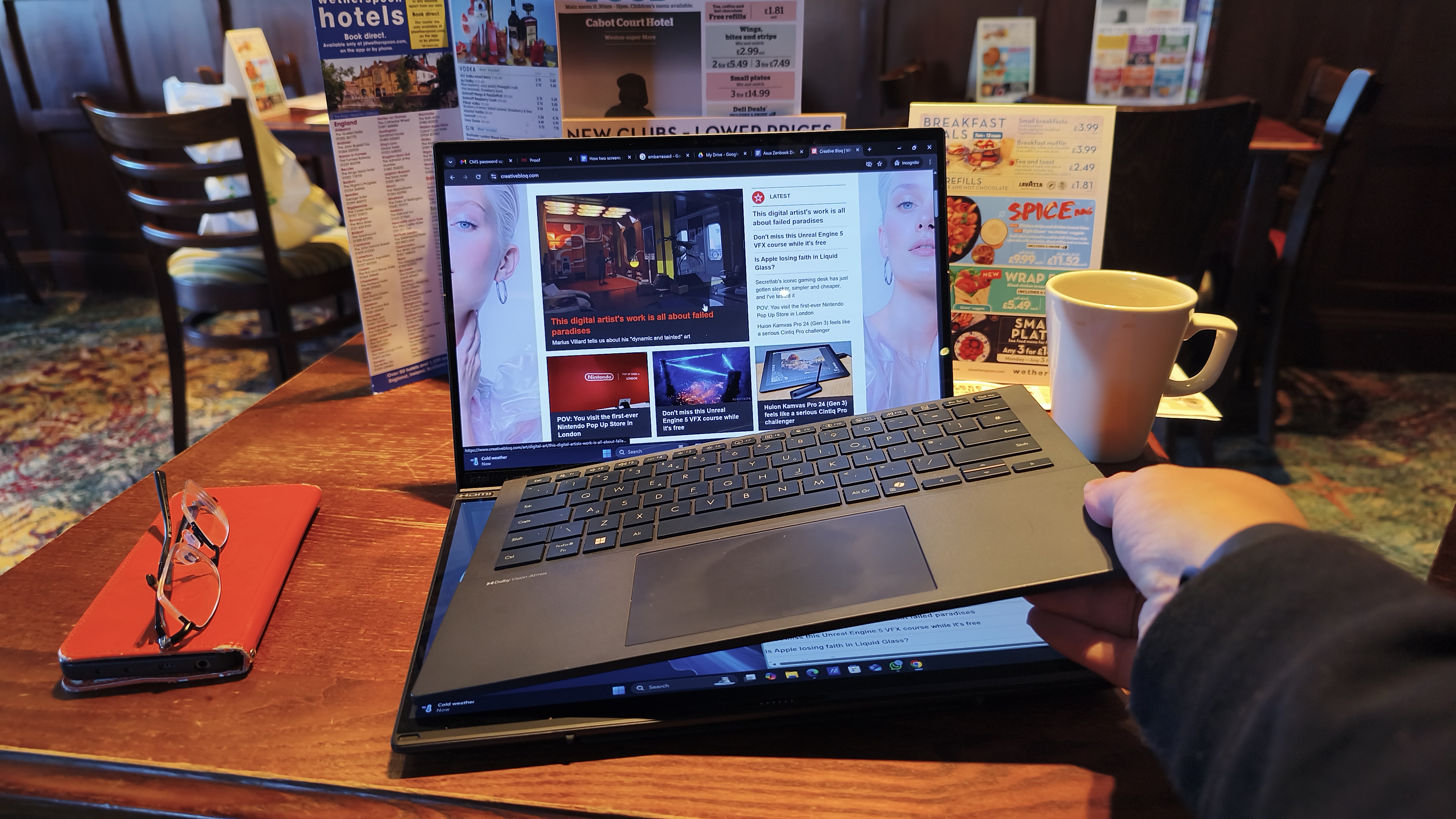 A hand is shown lifting the detachable keyboard from the base of the laptop, revealing the second touchscreen display beneath it.