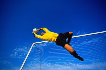 A soccer goalie is leaping in the air and has just caught the ball.