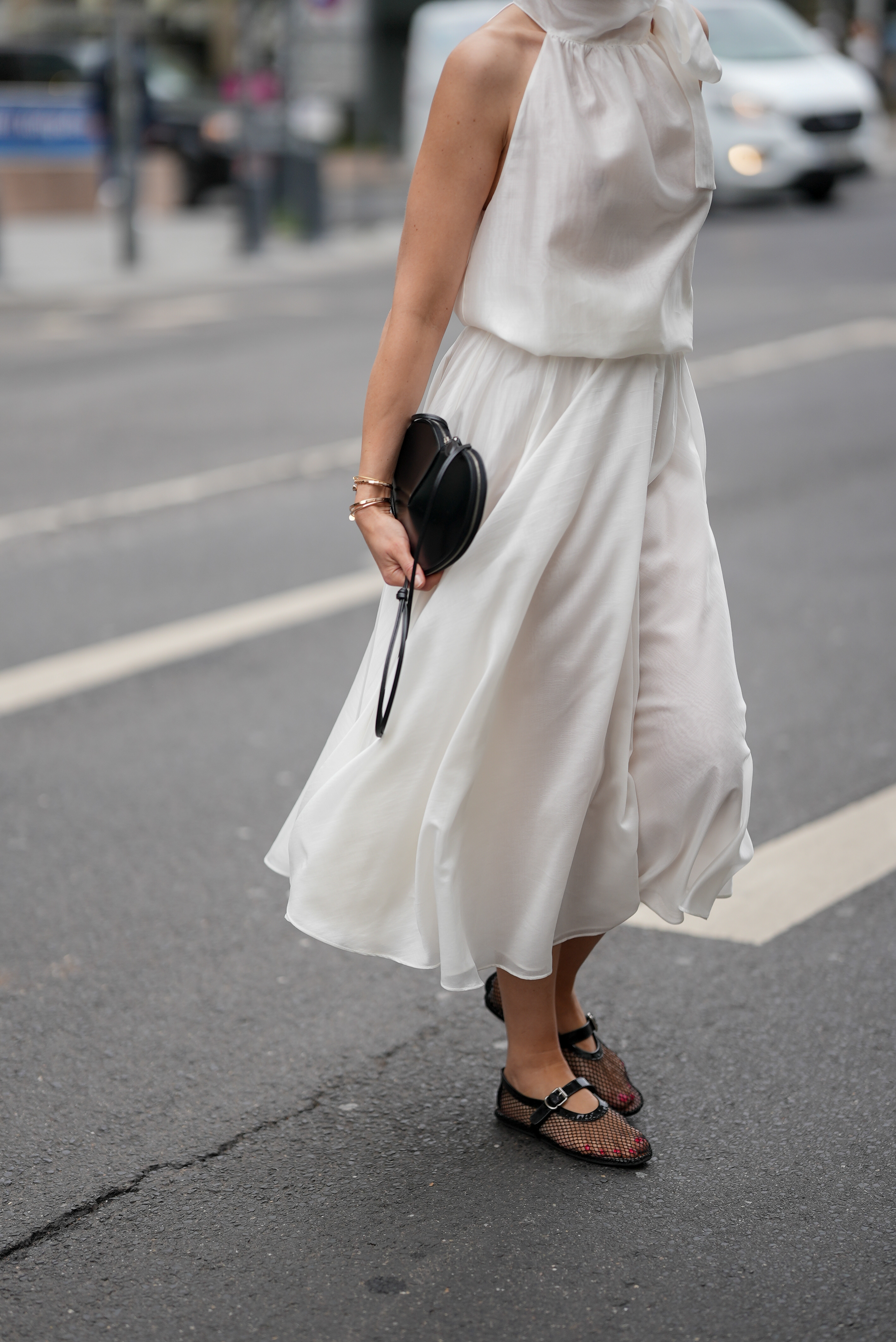 Patricia Wirschke is seen wearing a white two-piece consisting of a flowy midi skirt and a sleeveless blouse with high collar and tie detail at the neck from C.Wirschke Collection, a black heart-shaped calfskin leather Le Cœur bag from Alaïa, black patent leather ballerinas in mesh style with strap closure from Alaïa, a golden Juste un Clou bracelet from Cartier, a yellow golden Serpenti Viper bracelet with snake-like design from Bvlgari, a yellow golden Love bracelet from Cartier, on May 27, 2025 in Dusseldorf, Germany