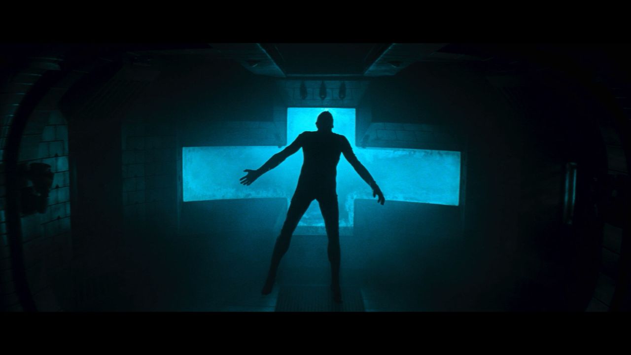 A human figures is standing with their arms and legs stretched outwards in front of a big blue plus sign.