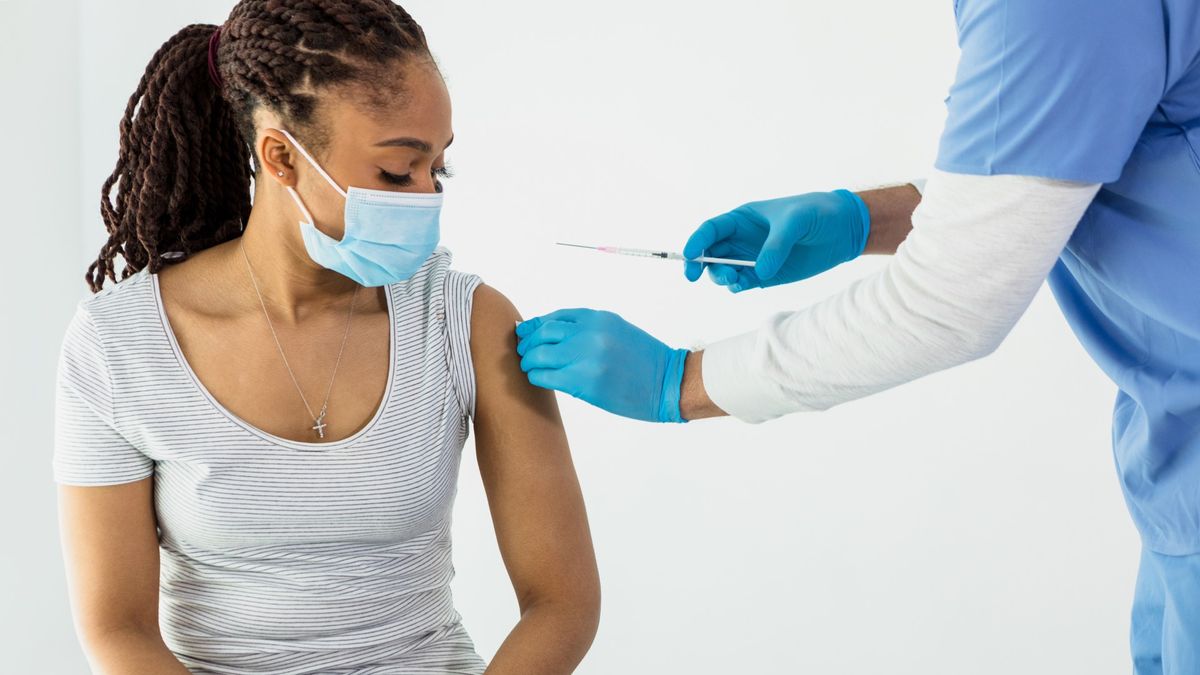 Person wearing a blue face mask sits and watches a nurse who is preparing their arm for vaccination