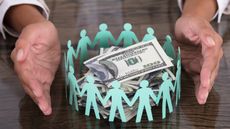 A pair of hands surround a pile of cash that's surrounded by paper cut-outs of people.