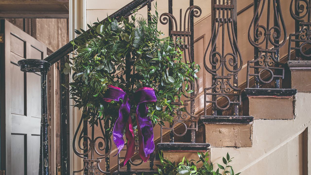 A foliage wreath with a purple bow hung on a staircase