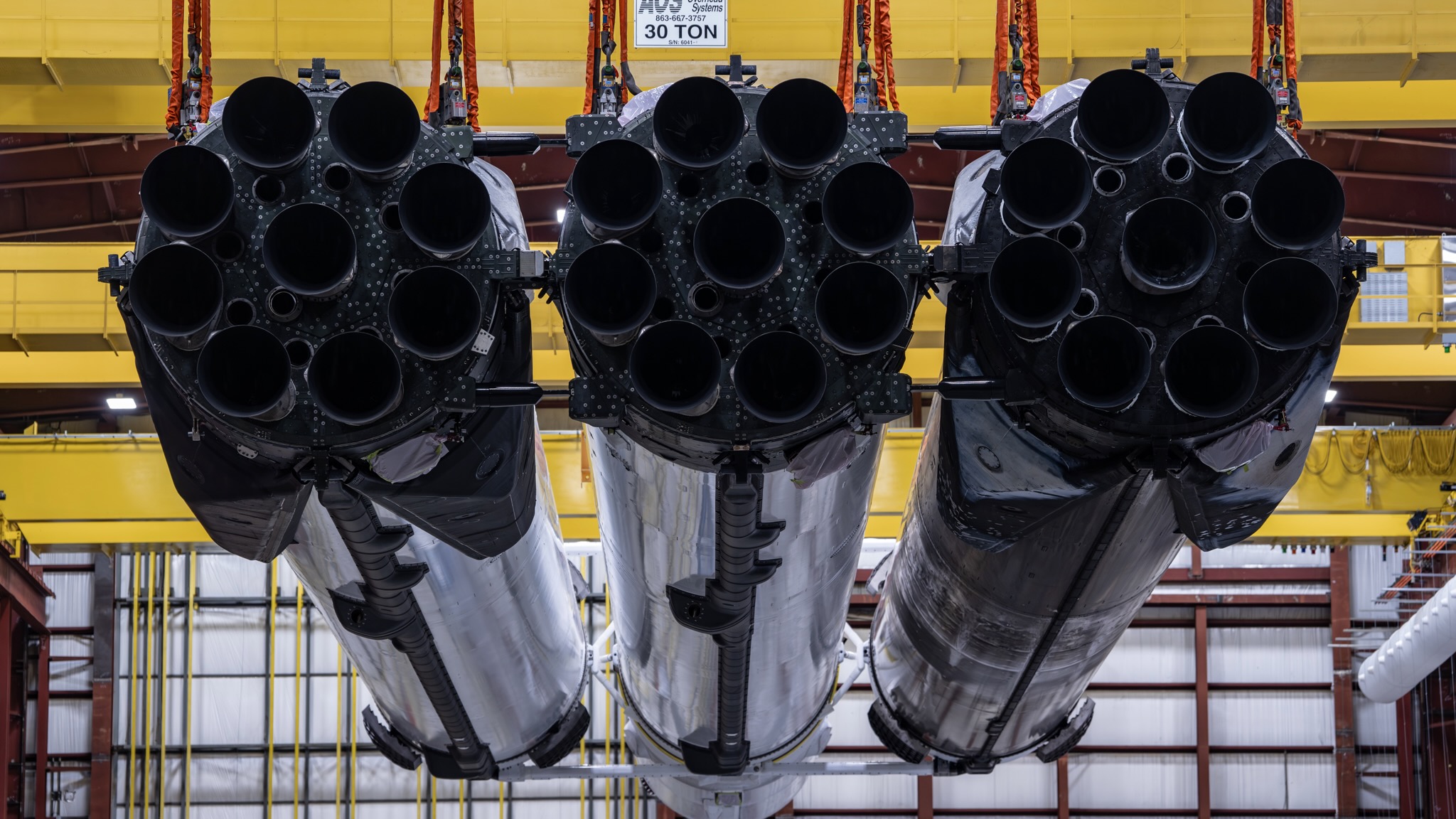 three large, linked-up silver rockets are seen suspended in a large hangar in a horizontal position
