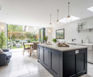 blue kitchen island with white worktop and open plan dining area leading to garden through bi-fold doors