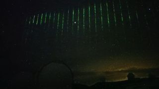 A time-lapse image of the green laser pulses flashing across the night sky.