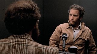 Richard Dreyfuss sits behind a table looking at a person opposite him