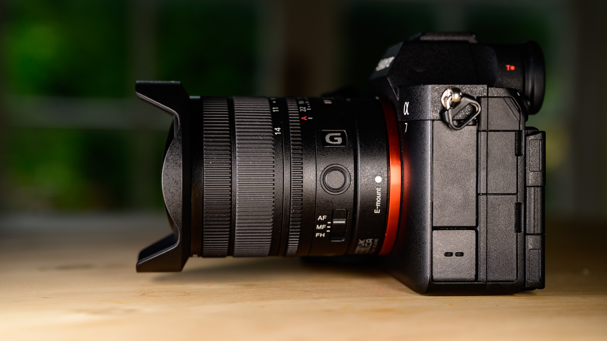 Sony FE 8-14mm F3.5 G fisheye lens attached to a Sony A7R V camera, on a wooden table, side profile