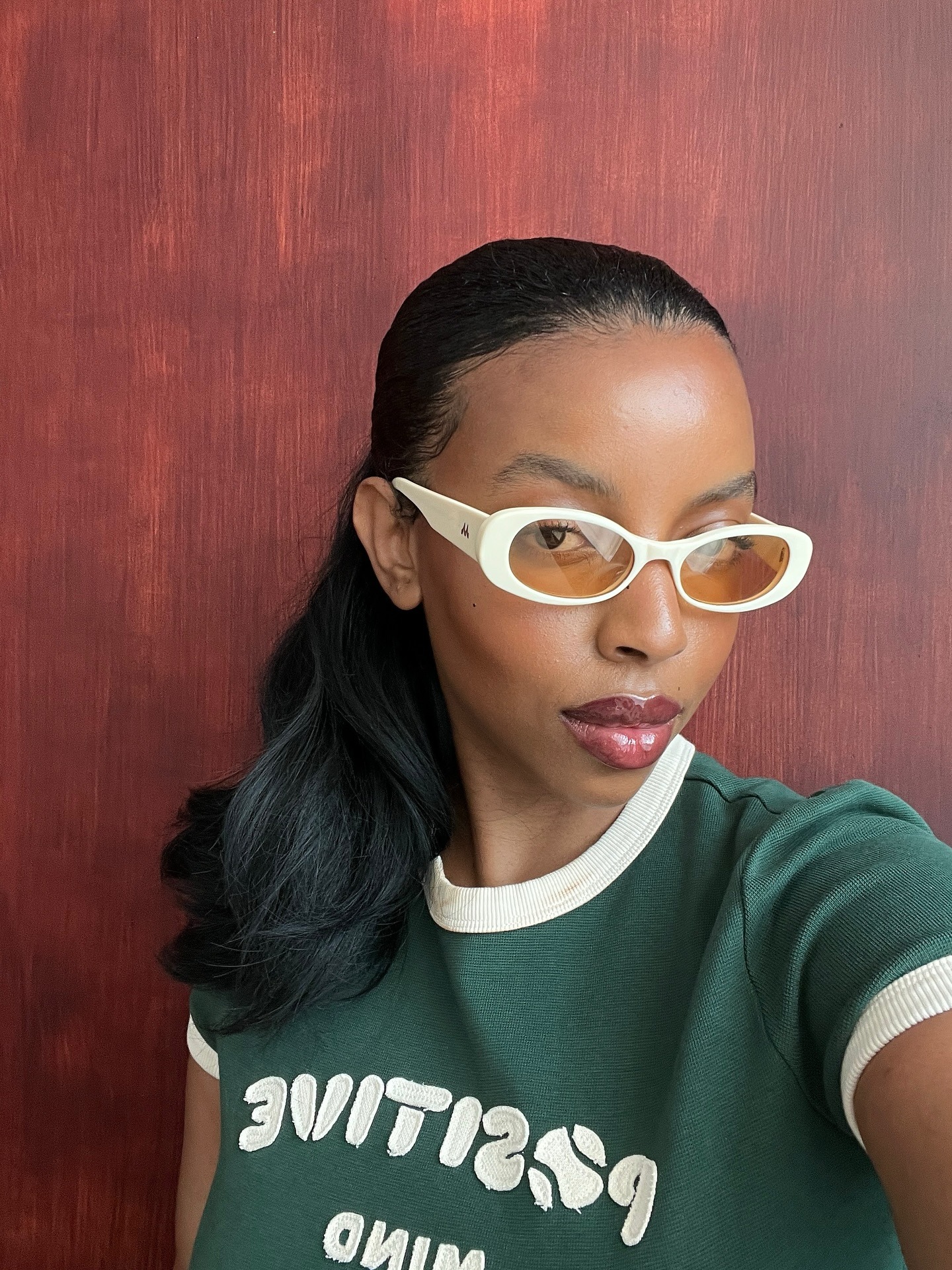A woman wearing white frame sunglasses and a green and white ringer tee.