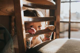 A young girl hiding behind a chair