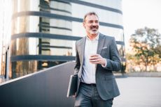 An older businessman stands outside his office.