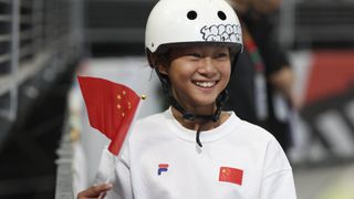 A young Chinese girl in a helmet waves the country's flag and smiles