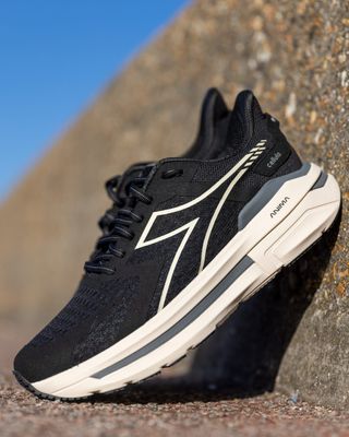 A pair of black and beige trainers is captured outdoors on a sunny day as it stands against a rock wall.