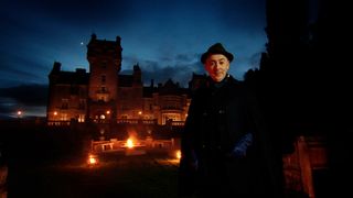 Alan Cumming standing in front of Ardross Castle at night in The Traitors US