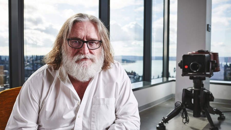 Gabe Newell looks into the camera, behind him is a prop of a turret from Team Fortress 2.