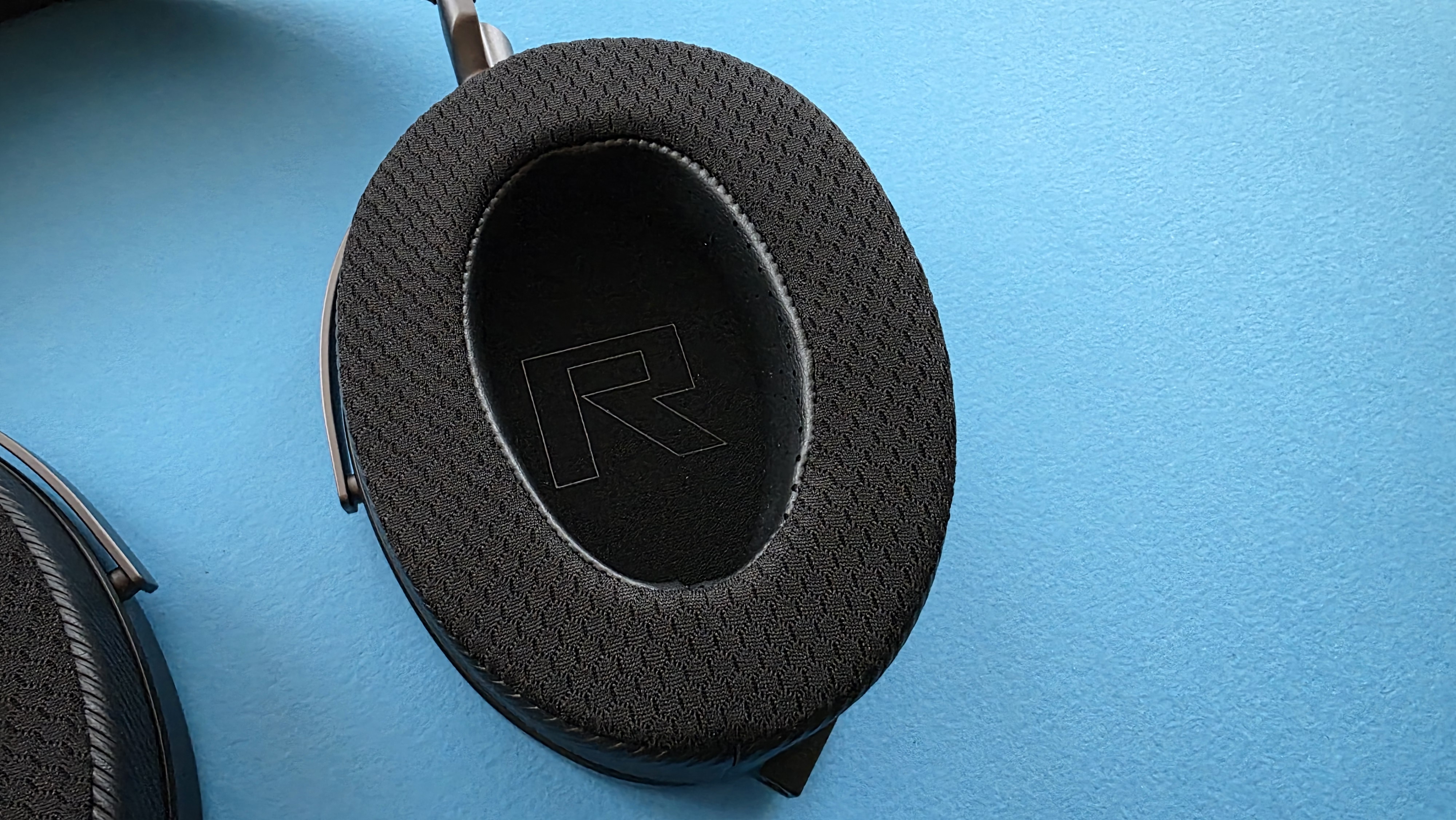 A pair of large, black, over-ear headphones with a striped grille design rests on a blue surface.