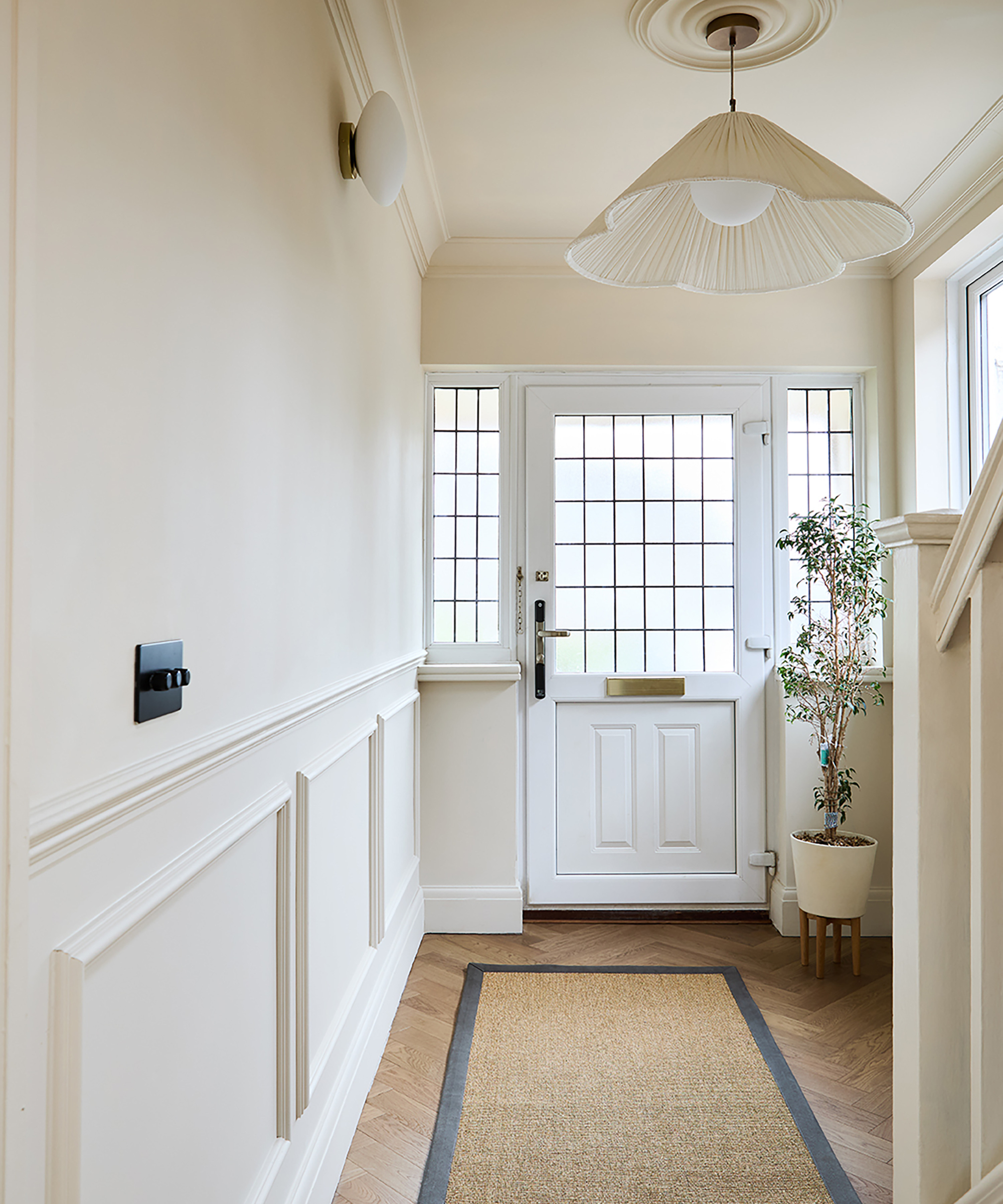 narrow hallway with wall panelling, half glazed door and windows and all painted white, wooden floor and jute rug
