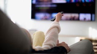 Male and female on a sofa, pointing a remote control at a TV