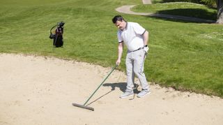 A golfer rakes a bunker